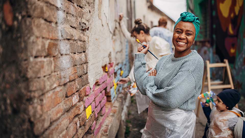 Group of male and female street artists drawing together on wall outdoors in city.