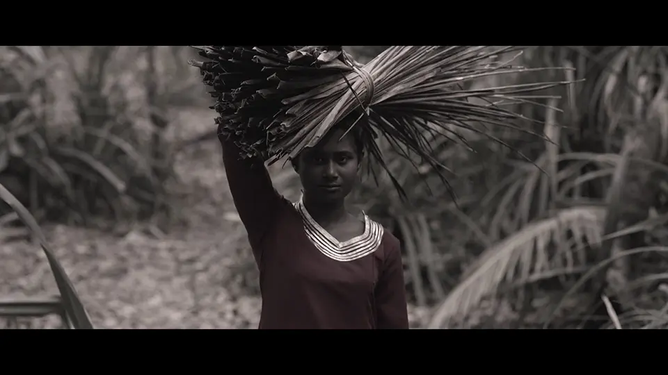Still shot of a woman with a bunch of dried leaves on her head from Shamin Nizam's movie Dhathuru