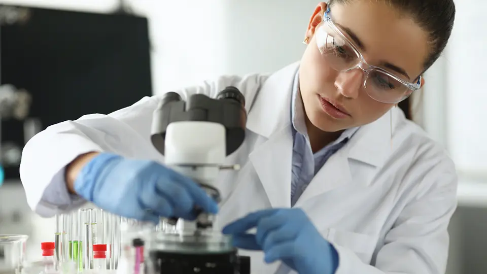 Woman scientist sitting in front of microscope in laboratory.