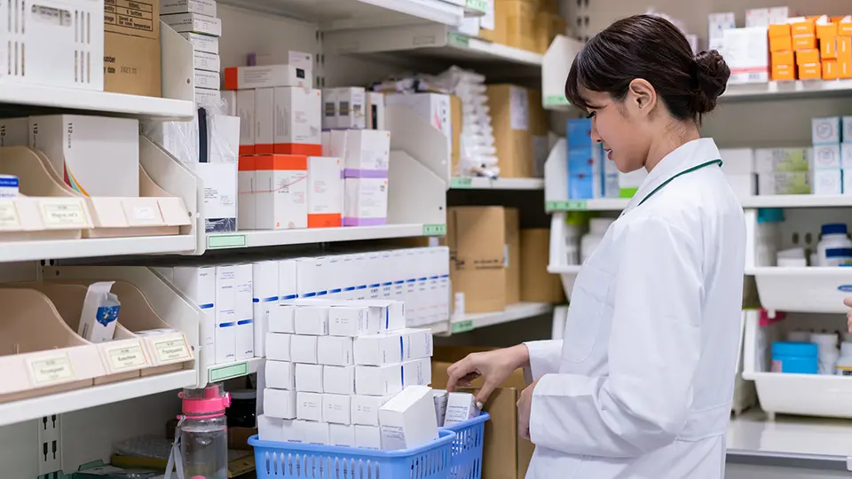 Female pharmacist arranging medicines on shelf.