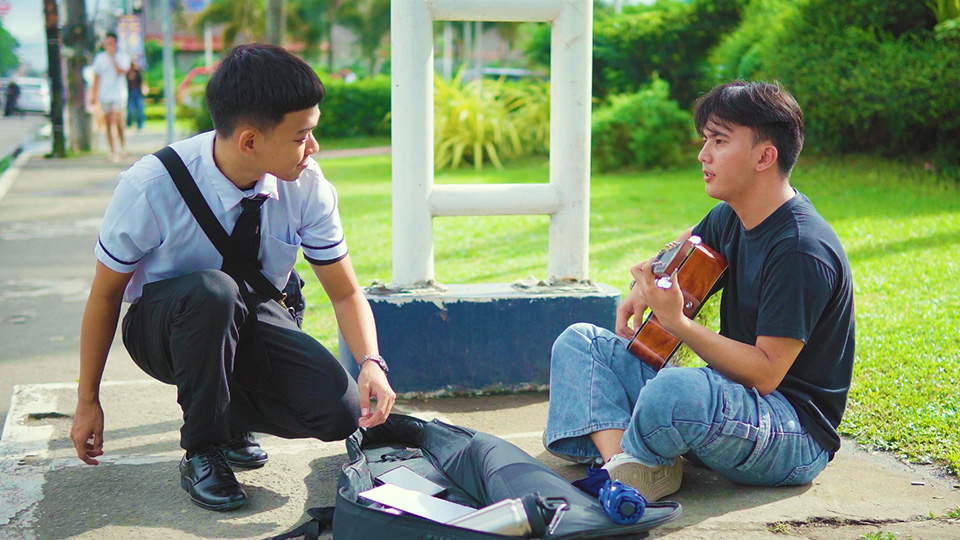 Seated guitarist playing in front of a student