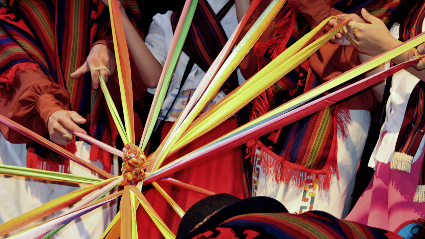 Indigenous women holding colorful ribbons woven together in a central point